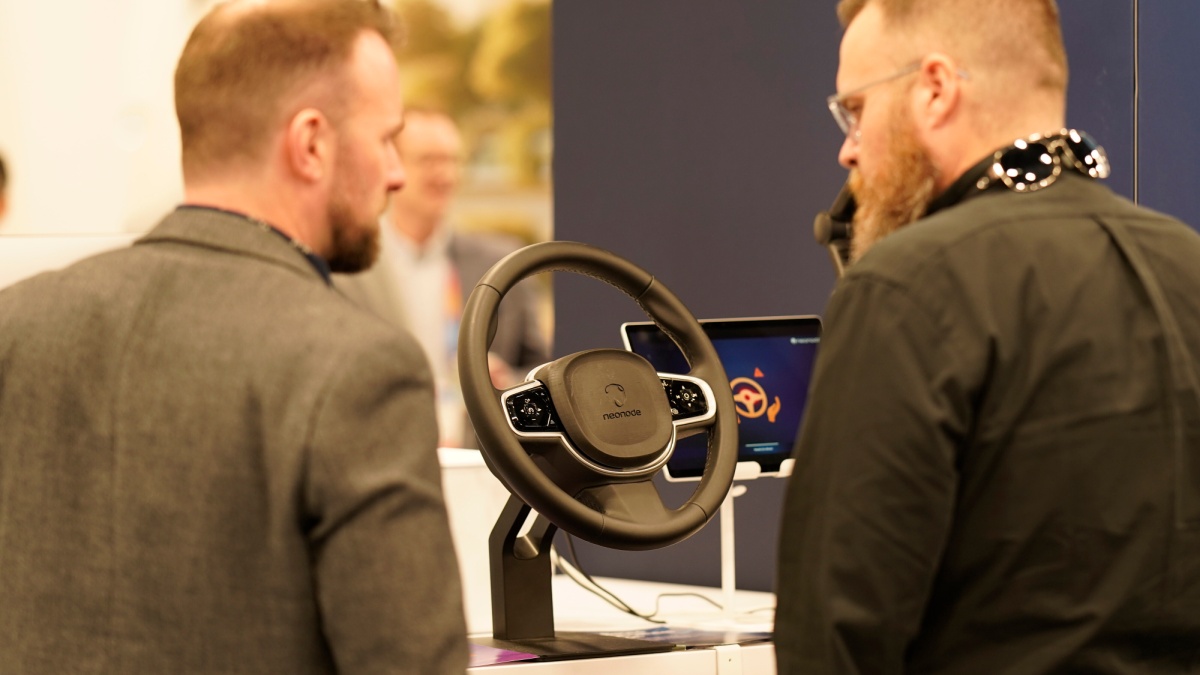 Two men discussing a steering wheel technology display at a trade show.