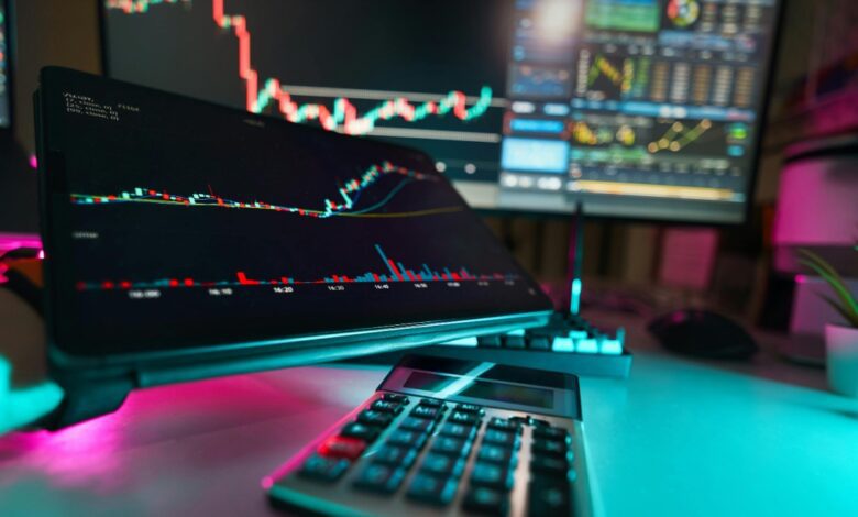 Stock market charts on tablet and computer screen with a calculator on the desk.