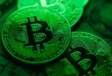 Close up of physical bitcoin tokens with circuit like patterns glowing under green lighting, placed on top of blurred paper currency in the background.