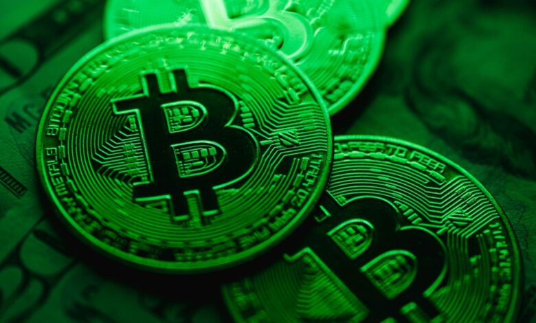 Close up of physical bitcoin tokens with circuit like patterns glowing under green lighting, placed on top of blurred paper currency in the background.