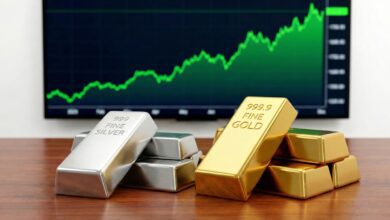 Stacks of silver and gold bars labeled "999 FINE SILVER" and "999.9 FINE GOLD" are displayed on a wooden surface in the foreground. In the background, a green upward-trending financial chart is shown on a screen, suggesting rising market prices for precious metals.