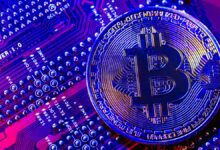 Close-up of a metallic bitcoin coin resting on a colorful computer circuit board with glowing blue and purple tones.