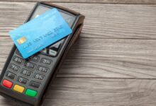 A blue credit card placed on a black payment terminal on a wooden surface.