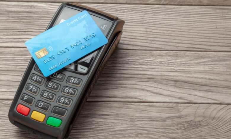 A blue credit card placed on a black payment terminal on a wooden surface.