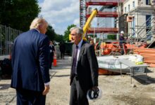 President Trump and Federal Reserve Chair Jerome Powell talk at the Fed Building construction site with scaffolding, equipment, and workers in the background.