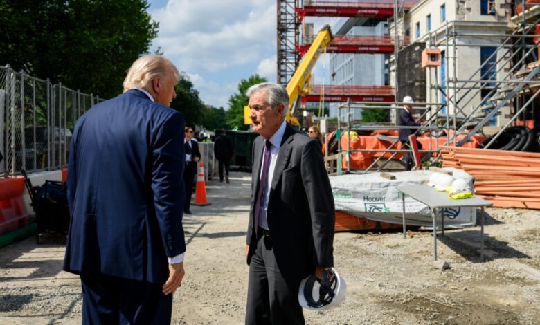President Trump and Federal Reserve Chair Jerome Powell talk at the Fed Building construction site with scaffolding, equipment, and workers in the background.